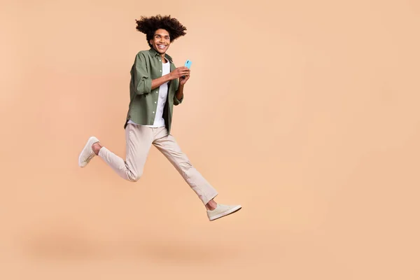 Full length body size view of attractive cheerful trendy guy jumping using device running isolated over beige pastel color background — Stock Photo, Image