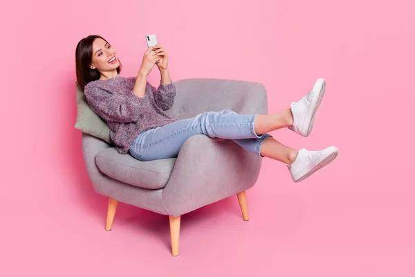 Portret van aantrekkelijke vrolijke meisje in fauteuil met behulp van apparaat gadget smm geïsoleerd over roze pastel kleur achtergrond — Stockfoto
