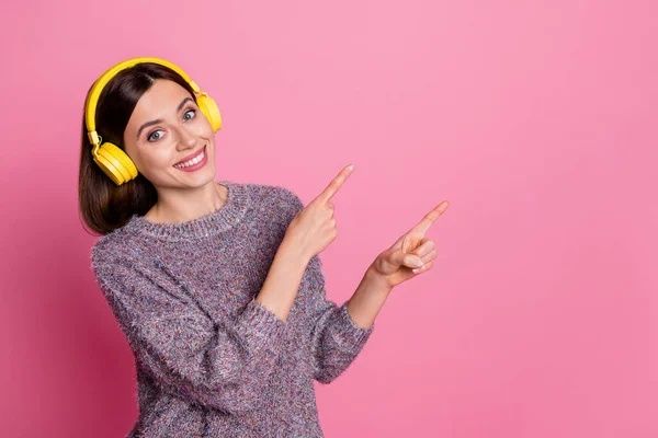 Foto av glänsande charmig dam klädd tröja hörlurar pekar tomt utrymme isolerad rosa färg bakgrund — Stockfoto