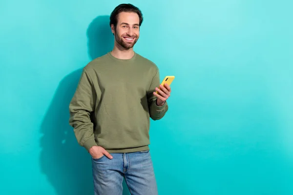 Foto van mooie brunet millennial guy houden telefoon dragen groene sweater geïsoleerd op teal kleur achtergrond — Stockfoto