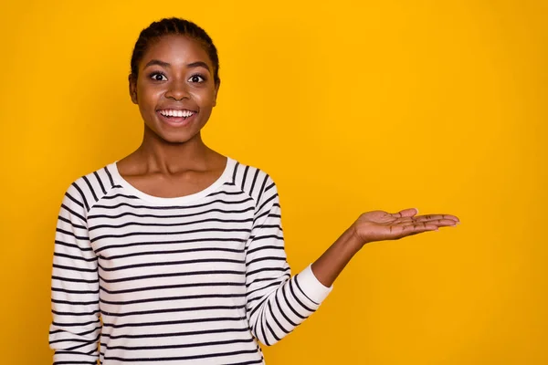 Fotografie mladé veselá dívka držet ruku přítomný produkt promotér navrhnout izolované přes žlutou barvu pozadí — Stock fotografie