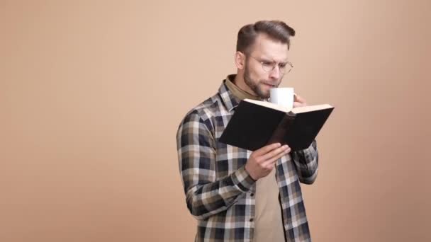 Inteligente cara hipster ler livro didático bebida caneca isolado pastel cor fundo — Vídeo de Stock