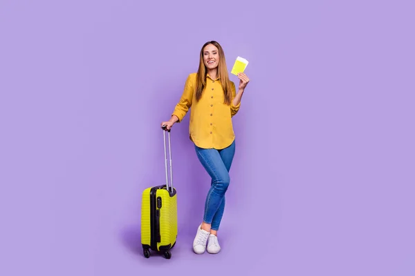 Изображение прекрасной девушки в полный рост в аэропорту в ожидании рейса, задержка багажа и билеты изолированы на фиолетовом фоне — стоковое фото