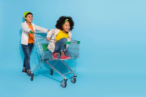 Full length body size view of small little friends friendship riding cart having fun isolated over bright blue color background — ストック写真