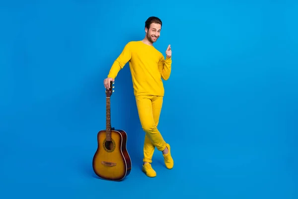 Повнометражний вигляд на тіло привабливого веселого хлопця, який тримає гітару, вказуючи на вас ізольовано на яскраво-блакитному фоні — стокове фото