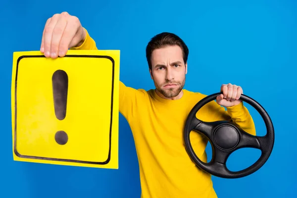 Portrait of attractive serious guy holding steering wheel exclamation sign warn isolated over bright blue color background — ストック写真