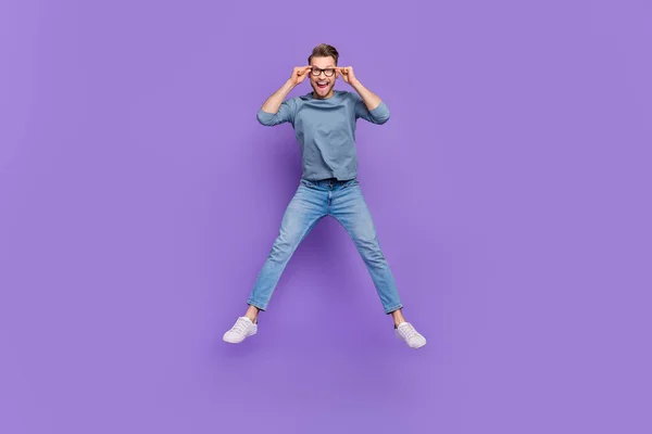 Фото веселого взволнованного парня в очках в серой рубашке, прыгающего высоко изолированного фиолетового цвета фона — стоковое фото