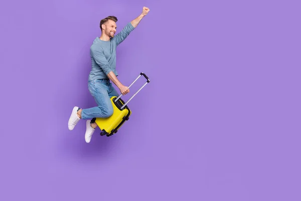 Фото збудженого крутого хлопця, одягненого в сіру сорочку, що стрибає з високим кулаком для багажу порожній простір ізольований фіолетовий кольоровий фон — стокове фото