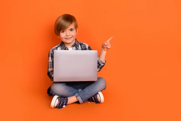 Pełnowymiarowe zdjęcie młodego chłopca wskazują palcem pustej przestrzeni polecam laptop promo izolowane na pomarańczowym tle koloru — Zdjęcie stockowe