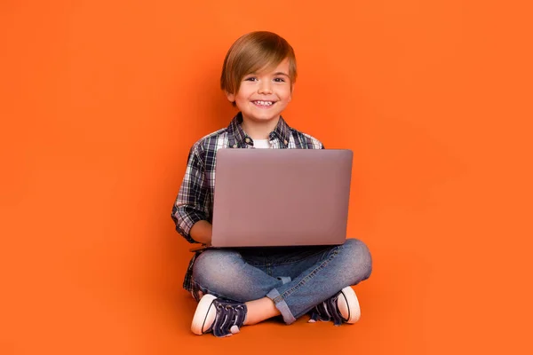 Pełny rozmiar zdjęcie młodego chłopca siedzieć podłogi używać laptopa badania online izolowane na pomarańczowym tle koloru — Zdjęcie stockowe
