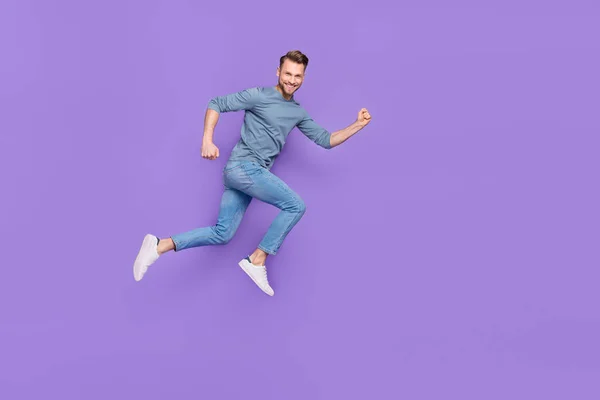 Photo of excited attractive guy wear grey shirt running fast jumping high empty space isolated violet color background — ストック写真