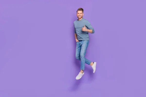 Foto de cara muito doce usar camisa cinza pulando alta caminhada mostrando polegar para cima espaço vazio isolado cor violeta fundo — Fotografia de Stock