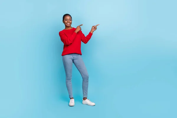 Foto de tamaño completo de dulce joven morena mujer índice promo desgaste camisa jeans zapatillas aisladas sobre fondo azul —  Fotos de Stock