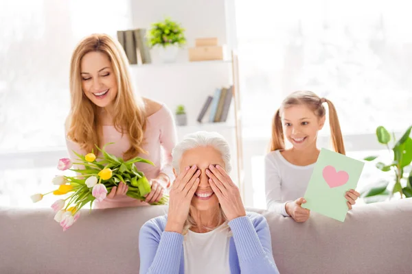 Porträtt av tre positiva idylliska människor gratulera tillfälle färska blommor handgjorda kort hus inomhus — Stockfoto