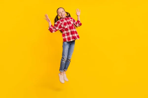 Foto de colegiala dulce excitado usar camisa a cuadros saltando alto espacio vacío aislado color amarillo fondo —  Fotos de Stock