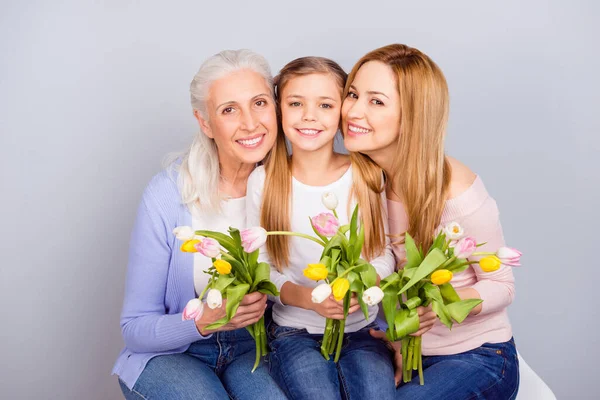 Ritratto di tre idilliache persone positive sedute abbracciare tenere tulipani freschi isolati su sfondo di colore grigio — Foto Stock