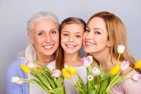 Foto de tres alegres personas amistosas sostienen tulipanes frescos radiantes sonrisa aislada en el fondo de color gris —  Fotos de Stock