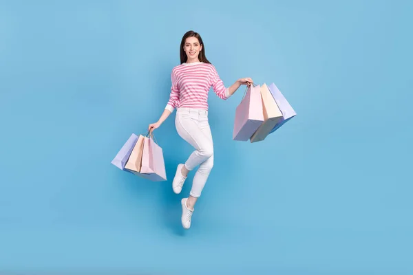 파란 배경에 분리 된 점프 패키지를 들고 있는 쾌활하고 예쁜 여자 상점의 전체 크기 사진 — 스톡 사진