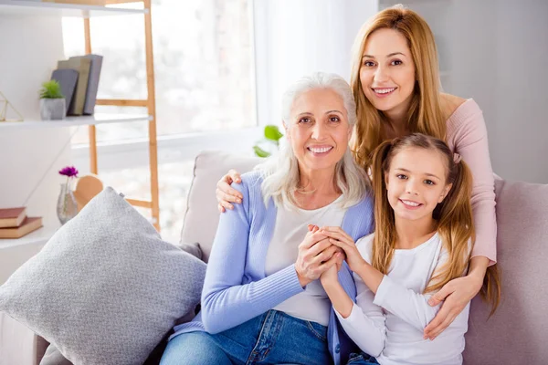 Porträt von drei freundlichen, gut gelaunten Frauen, die auf dem Sofa sitzen und Arme halten, um ihre Freizeit im Haus zu genießen — Stockfoto