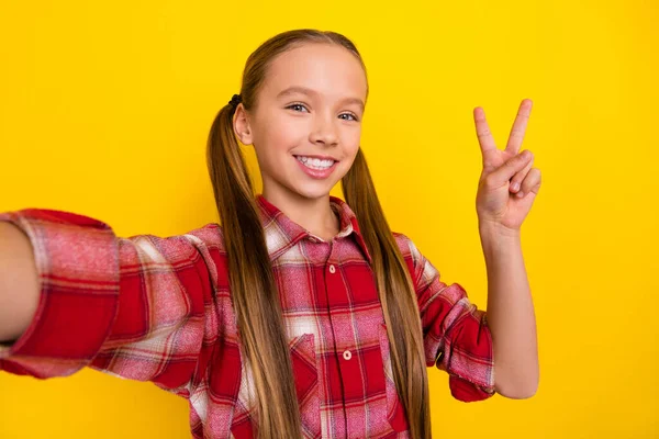 Foto av ganska rolig skolflicka bära rutig skjorta inspelning själv video visar v-tecken isolerad gul färg bakgrund — Stockfoto