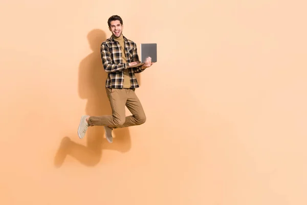 Full length body size view of attractive cheery guy jumping using laptop copy space eshop isolated on beżowy pastelowy kolor tła — Zdjęcie stockowe