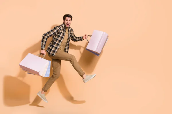 Vista completa del tamaño del cuerpo del atractivo chico loco alegre saltando llevando bolsas aisladas sobre fondo de color pastel beige — Foto de Stock