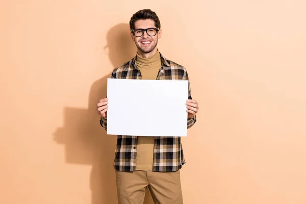Retrato de atractivo chico alegre especialista sosteniendo en las manos banner espacio de copia aislado sobre fondo de color pastel beige — Foto de Stock