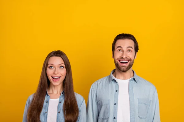 Foto de engraçado impressionado marido esposa usar camisas jeans olhando para cima espaço vazio isolado cor amarela fundo — Fotografia de Stock