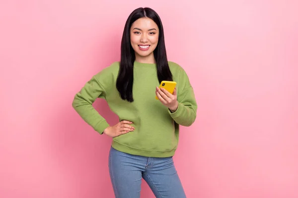 Foto de linda joven dama mantenga el uso de teléfono jersey verde aislado en el fondo de color rosa — Foto de Stock