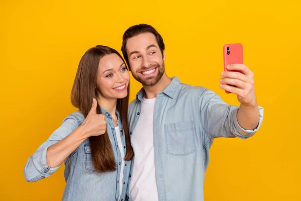 Foto de hooray milenar casal penteado marrom fazer selfie mostrar polegar-se desgaste jeans camisa isolada no fundo amarelo — Fotografia de Stock