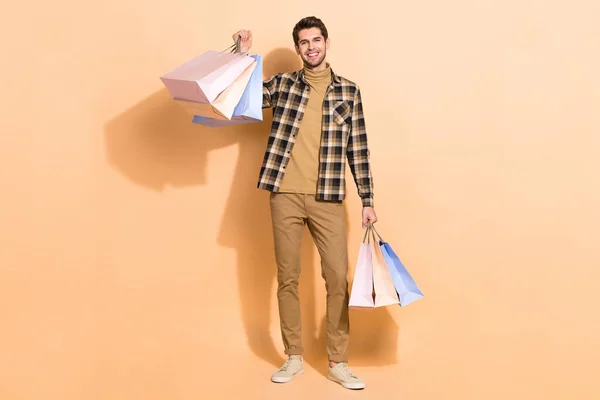 Vista completa del tamaño del cuerpo del atractivo chico alegre sosteniendo bolsas cosas nuevas aisladas sobre fondo de color pastel beige — Foto de Stock