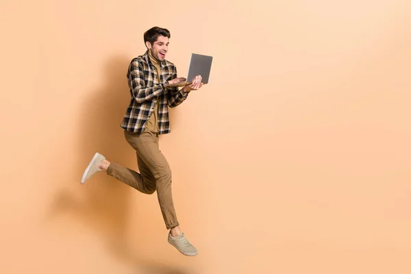 Full length body size view of attractive wesoły wykwalifikowany facet jumping using laptop copy space isolated on beżowy pastelowy kolor tła — Zdjęcie stockowe