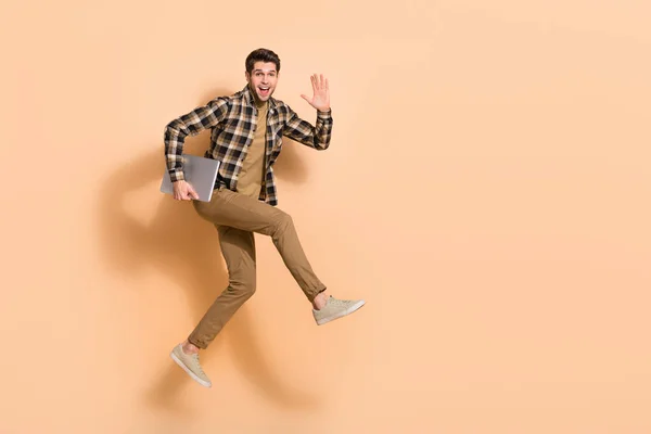 Full length body size view of attractive cheery guy jumping holding laptop waving hi isolated on beżowy pastelowy kolor tła — Zdjęcie stockowe