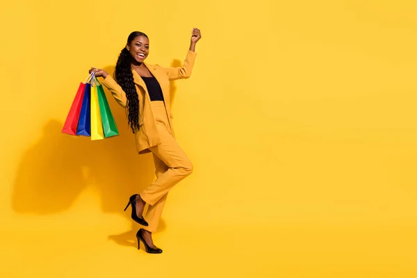 Foto de tamaño completo de señora joven cool hacer compras usar chaqueta pantalones stilettos aislados sobre fondo amarillo — Foto de Stock