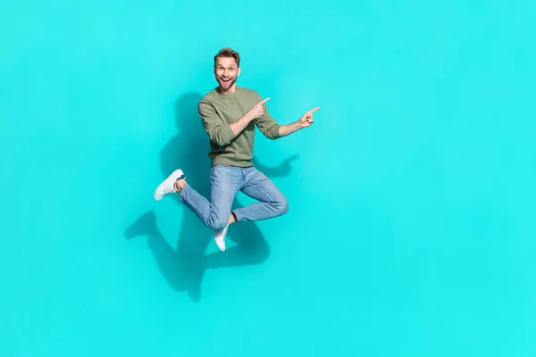 Foto de tamaño completo de millennial chico rubio índice de salto promo desgaste pantalones vaqueros zapatos aislados sobre fondo verde azulado — Foto de Stock