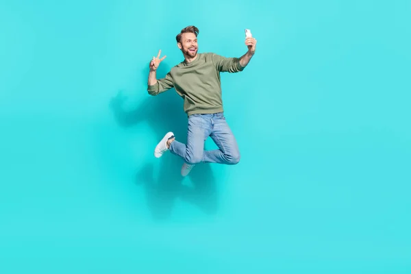 Full length profile photo of crazy blogger man jump hold telephone make selfie wear pullover isolated blue color background — ストック写真