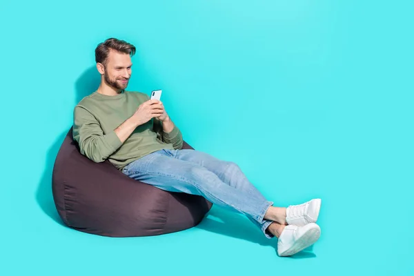 Foto de inteligente alegre agradable influencer hombre celebrar teléfono sentarse sillón desgaste jersey aislado color azul fondo —  Fotos de Stock