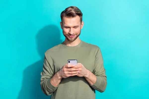 Foto de millennial loiro bonito cara segurar telefone desgaste cáqui pulôver isolado no fundo cor teal — Fotografia de Stock