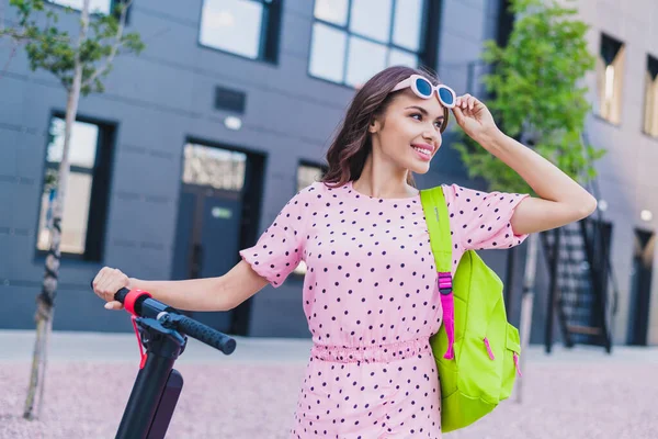 Retrato de atraente alegre sonhador ondulado menina equitação scooter passar férias visitando amigo ao ar livre — Fotografia de Stock