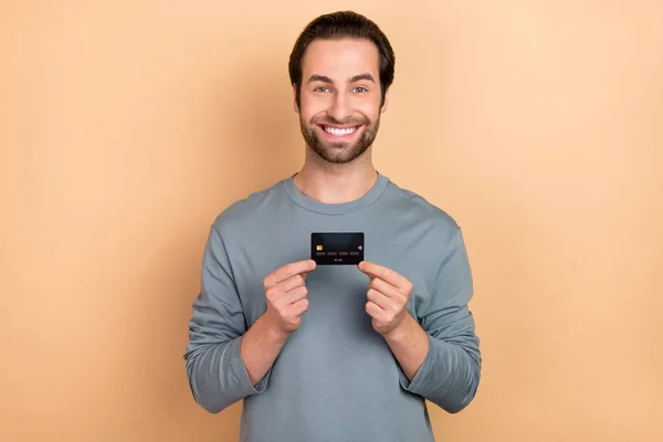 Foto do jovem homem alegre segurar o salário benefício de renda do cartão bancário isolado sobre fundo de cor bege — Fotografia de Stock