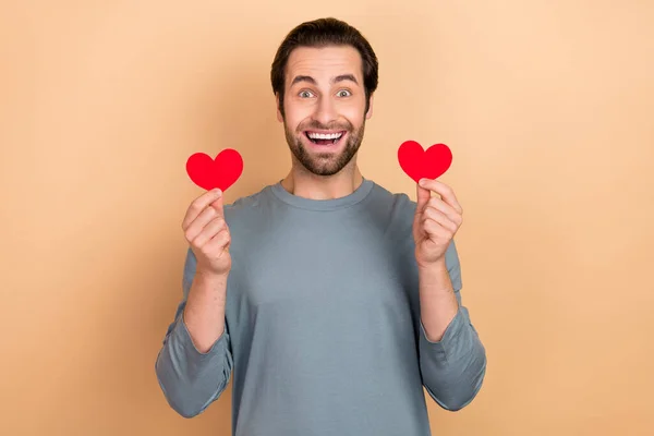 Fotografie mladého vzrušeného muže držet ruce malé srdce tvar romantické srdce izolované přes béžové barvy pozadí — Stock fotografie
