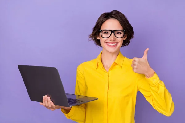 写真のCEO若い女性ホールドノートパソコン親指アップ着用黄色の衣装アイウェア隔離された紫色の背景 — ストック写真