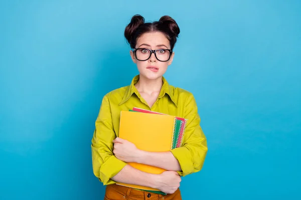 Portrait of puzzled young lady hold copybooks biting lip look camera isolated on blue color background — Stock Photo, Image