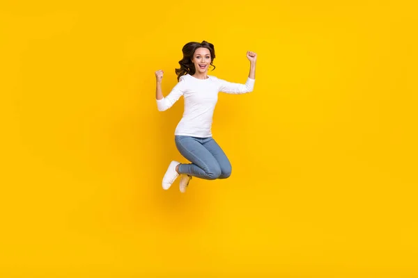 Foto de dulce afortunada mujer usar camisa blanca levantando puños saltando alto aislado color amarillo fondo —  Fotos de Stock