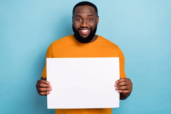 Fotografie legrační sladký chlap oblečený oranžové tričko drží bílý papír list prázdný prostor izolované modré barvy pozadí — Stock fotografie