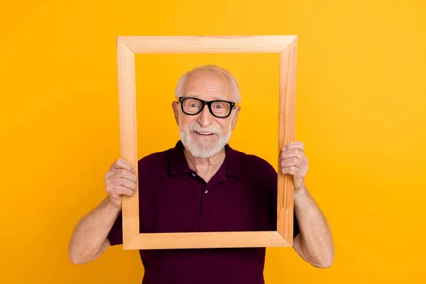 Bild av glad mogen man håller trä ram skytte ögonblicksbild isolerad över gul färg bakgrund — Stockfoto