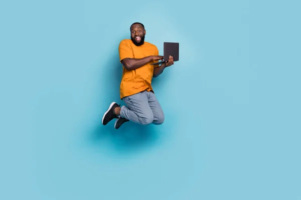 Foto de cara bonito chocado usar laranja t-shirt saltando alta digitação moderno dispositivo isolado azul cor de fundo — Fotografia de Stock