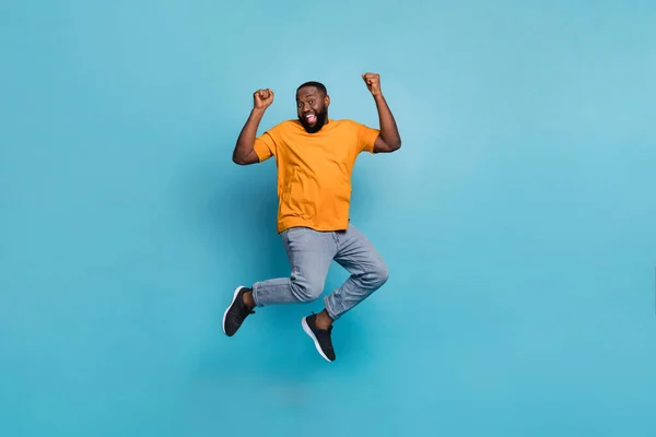 Foto de cara sorte atraente vestido laranja t-shirt pulando altos punhos em ascensão isolado azul cor de fundo — Fotografia de Stock