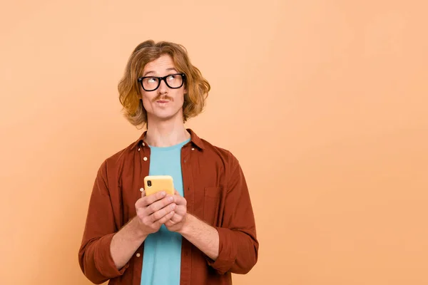 Ritratto di attraente ragazzo mentalità utilizzando dispositivo scegliendo spazio copia smm post isolato su sfondo colore pastello beige — Foto Stock