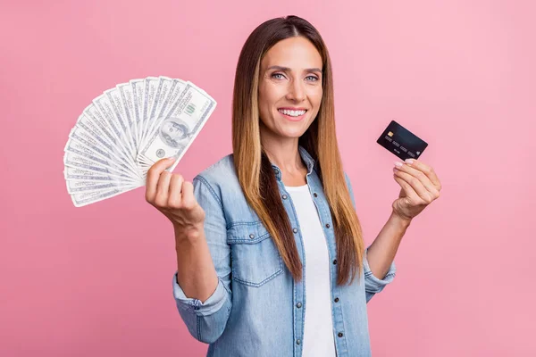 Foto di giovane donna allegra tenere dollari contanti reddito della carta di credito isolato su sfondo di colore rosa — Foto Stock